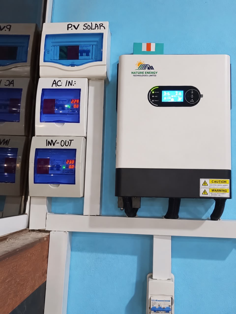 Inverter with labelled PV, AC input and inverter output distribution boards on a plant room wall
