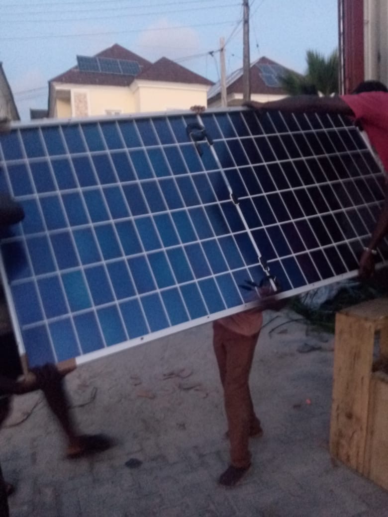 Technicians carrying a large solar panel across a compound at dusk